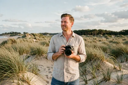 Photographe professionnel debout sur les dunes de sable des Landes avec son appareil photo, paysage côtier atlantique en arrière-plan
